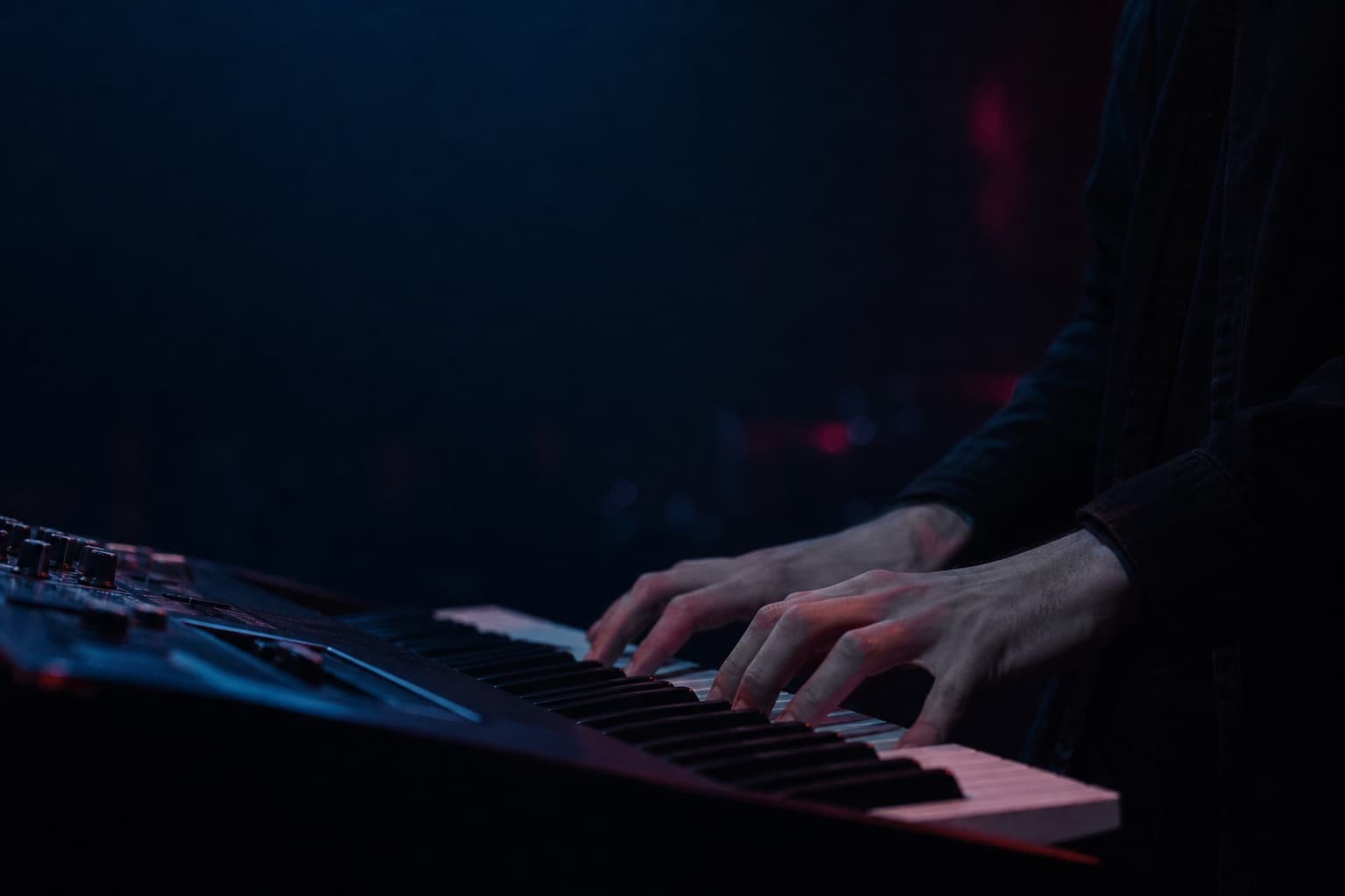 Hands playing a keyboard under dark stage lighting